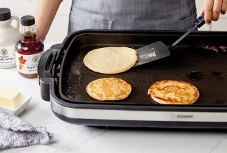 Baker flipping a batch of pancakes on an electric griddle